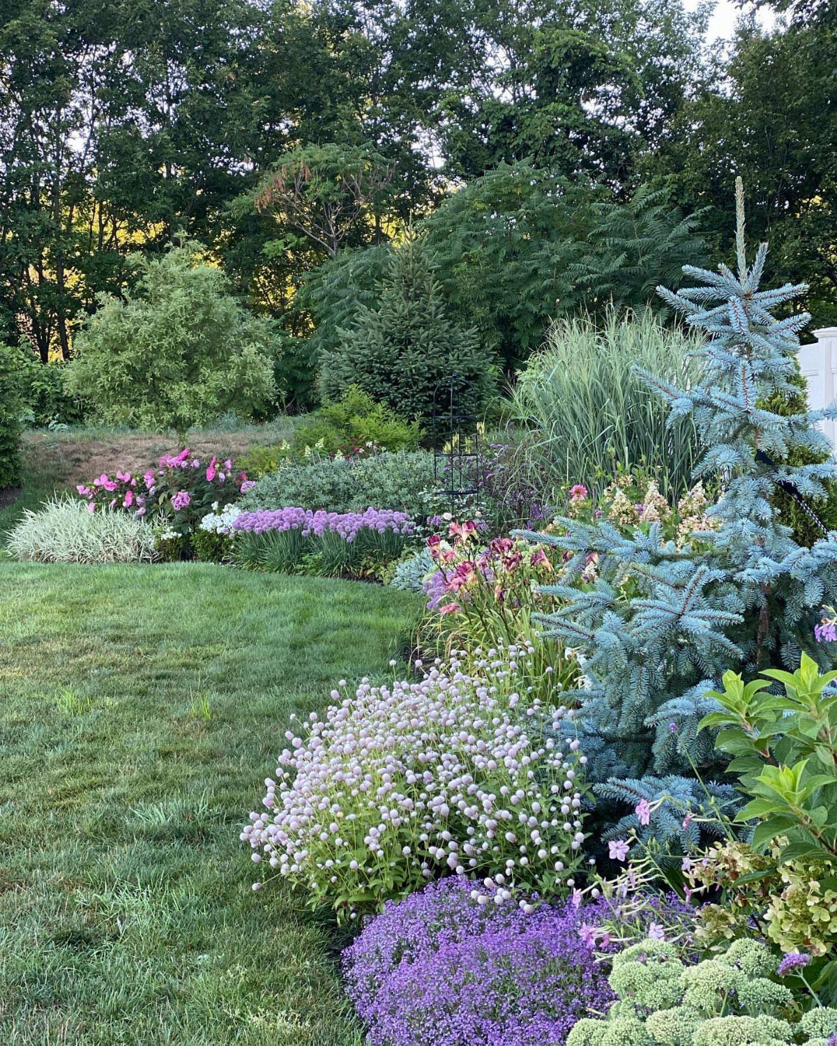 25 Creative and Gardening Ideas for Backyards Big or Small 15 Layered garden borders with colorful flowers and various green shrubs under a canopy of trees.