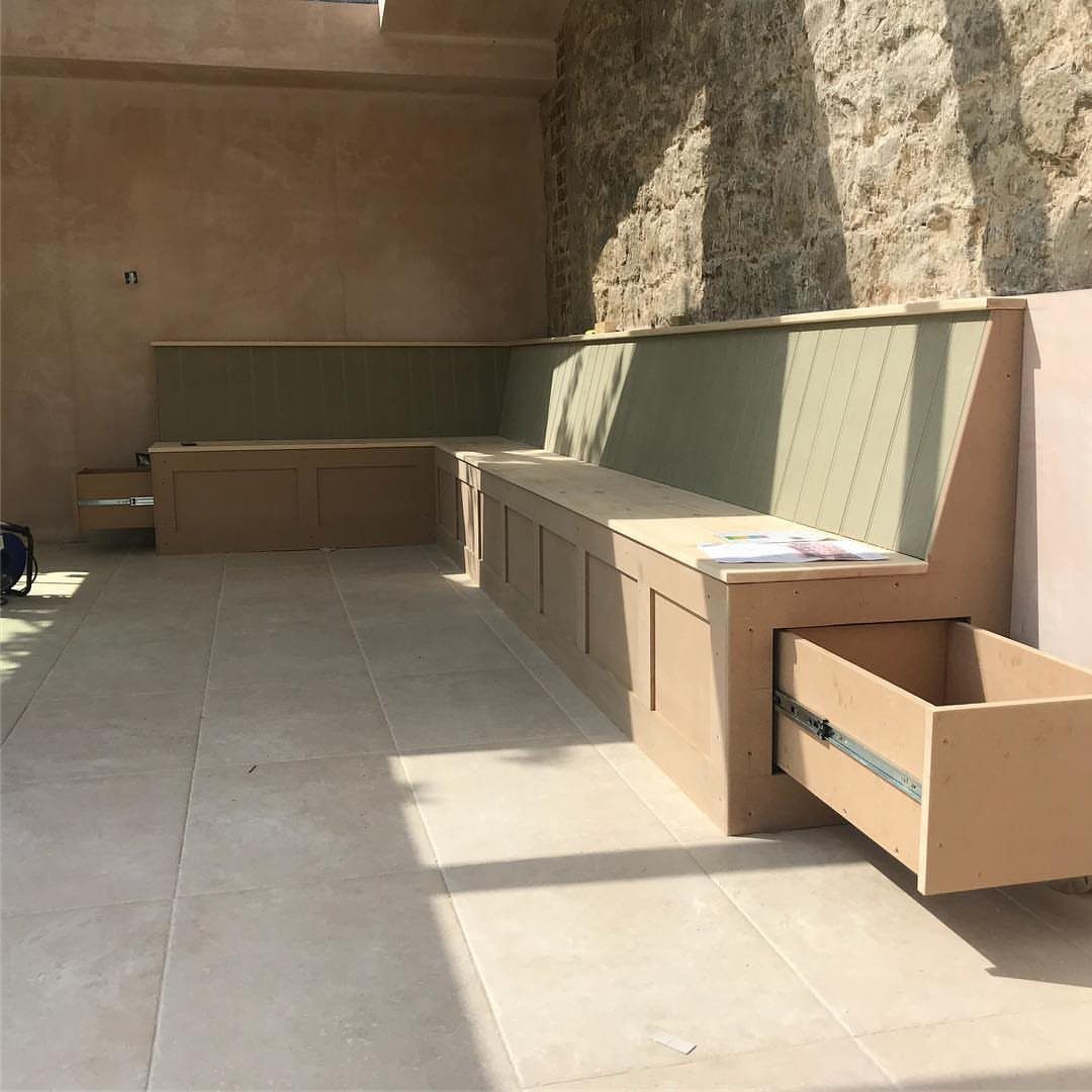 9 Deck Bench Seating Ideas for Storage, Planters and Rail-Top Perches 6 Built-in tan wooden corner bench with storage drawers on a stone patio.