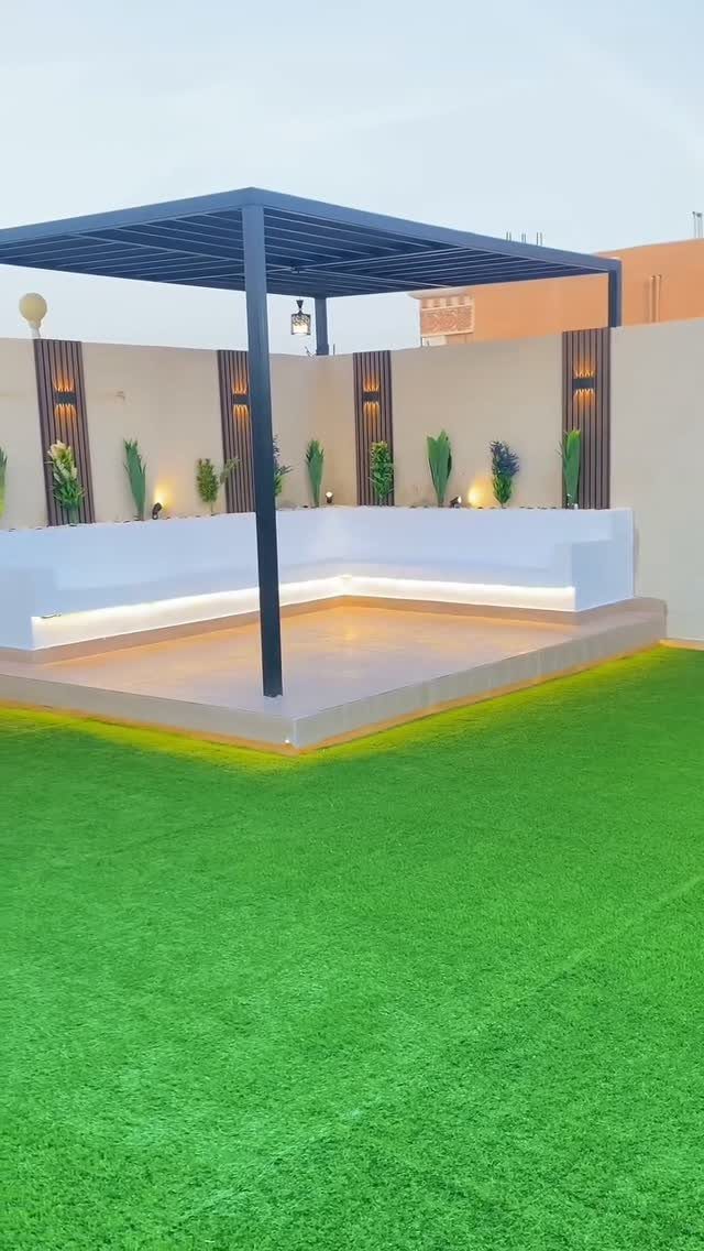 9 Deck Bench Seating Ideas for Storage, Planters and Rail-Top Perches 4 White built-in corner bench seating under a dark pergola on a raised platform next to green grass.