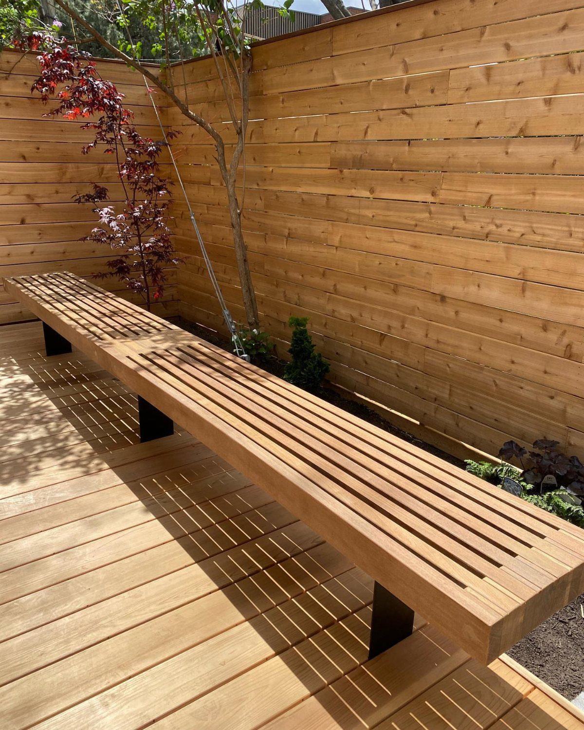 9 Deck Bench Seating Ideas for Storage, Planters and Rail-Top Perches 2 A long wooden slat bench supported by dark metal brackets on a sunny wooden deck.