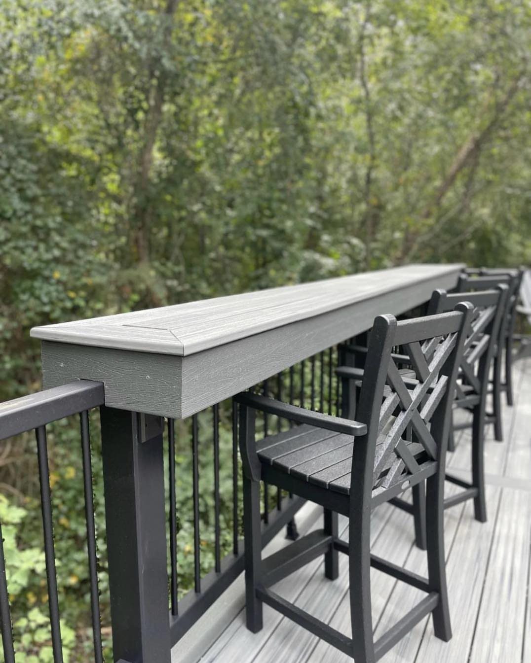 9 Deck Bench Seating Ideas for Storage, Planters and Rail-Top Perches 7 A grey wooden bar counter integrated into a black metal deck railing with black stools.