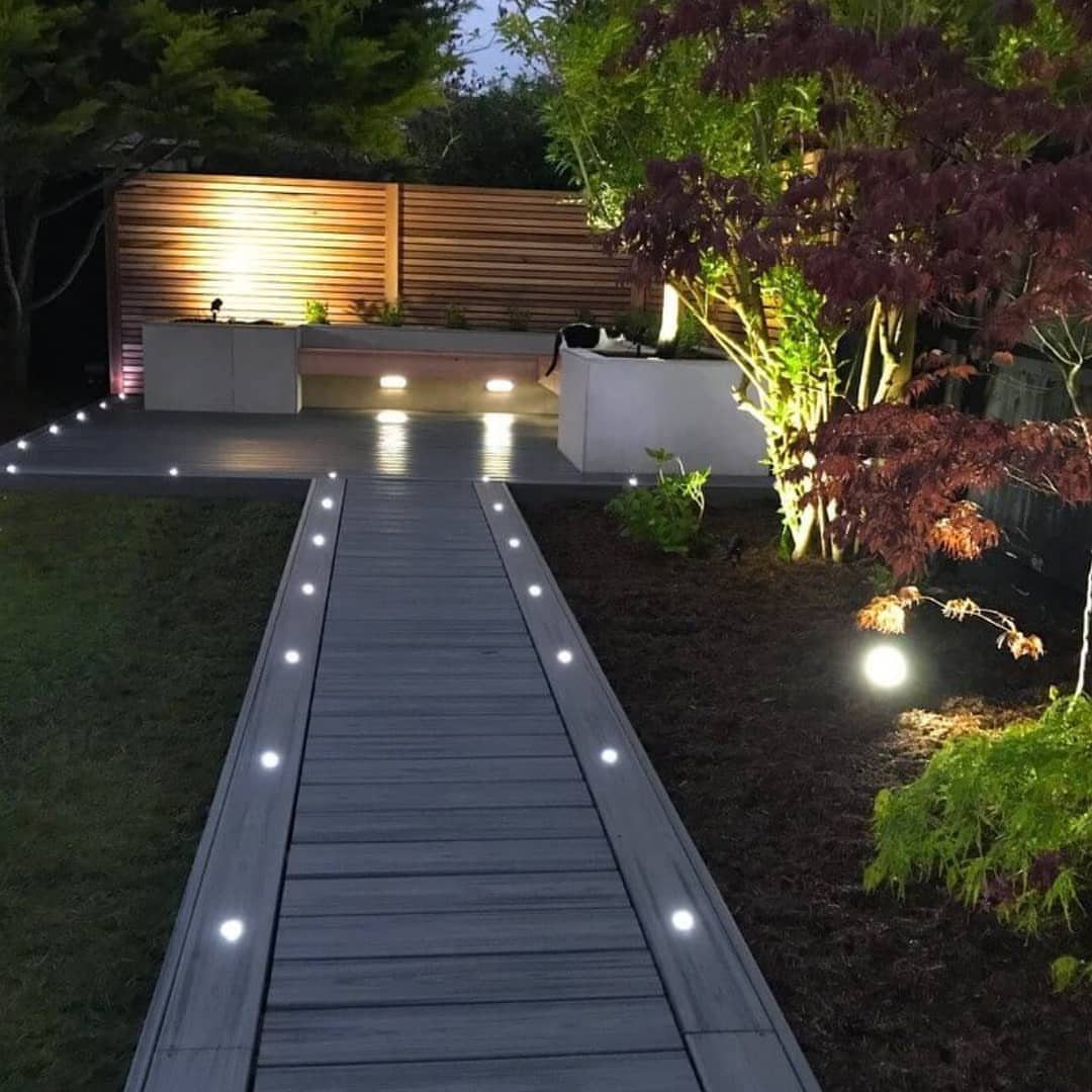 12 Deck Floor Design Ideas for Picture-Frame Borders to Patterned Layouts 2 Small circular LED lights embedded in a wooden deck walkway leading to a patio at night.