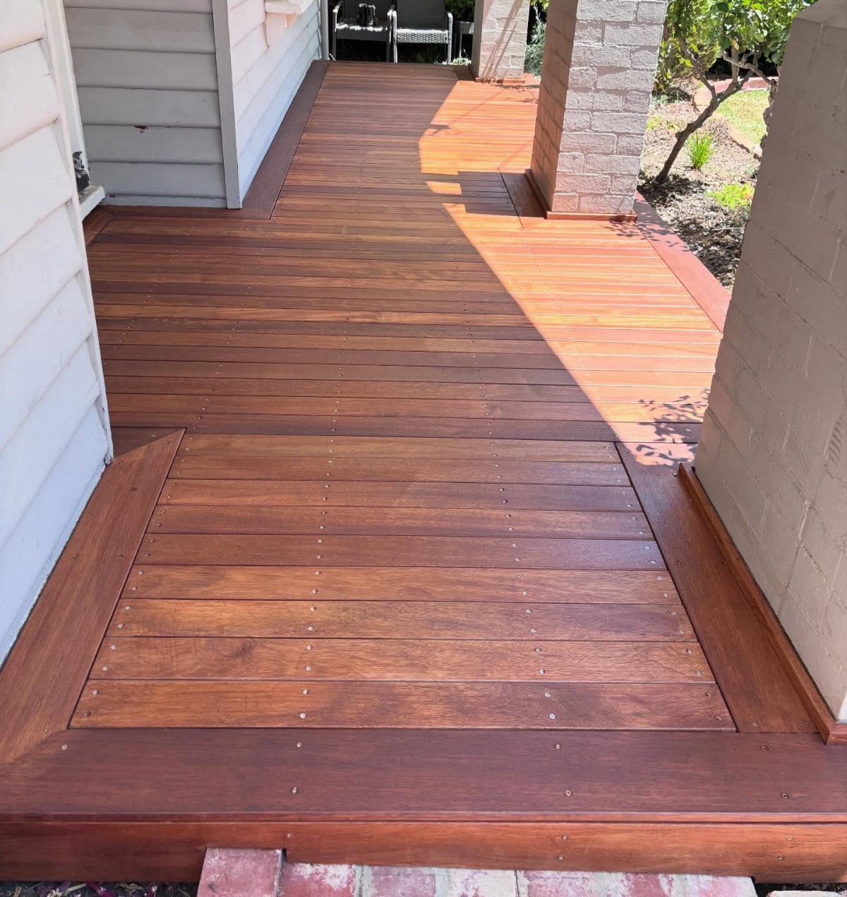 12 Deck Floor Design Ideas for Picture-Frame Borders to Patterned Layouts 7 Reddish-brown timber deck with a decorative rectangular inlay pattern next to a house.