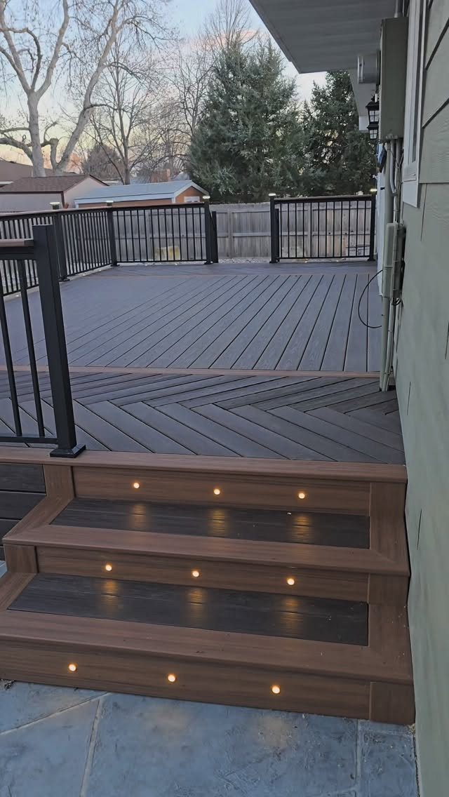 12 Deck Floor Design Ideas for Picture-Frame Borders to Patterned Layouts 9 A dark brown composite deck featuring a herringbone pattern and integrated LED step lights.
