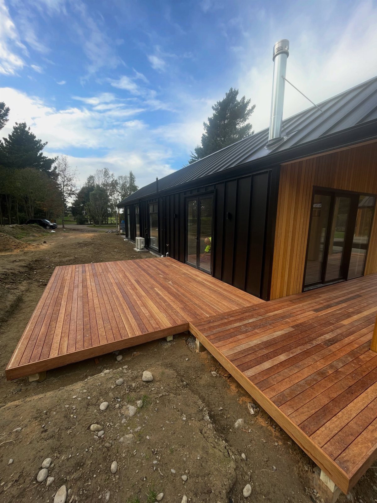 12 Deck Floor Design Ideas for Picture-Frame Borders to Patterned Layouts 8 A multi-level wooden deck with reddish-brown planks attached to a modern black house.