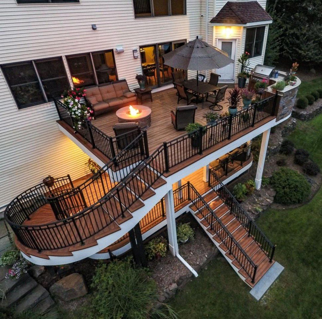 A multi-level wooden deck with black railings, featuring a fire pit and outdoor furniture.