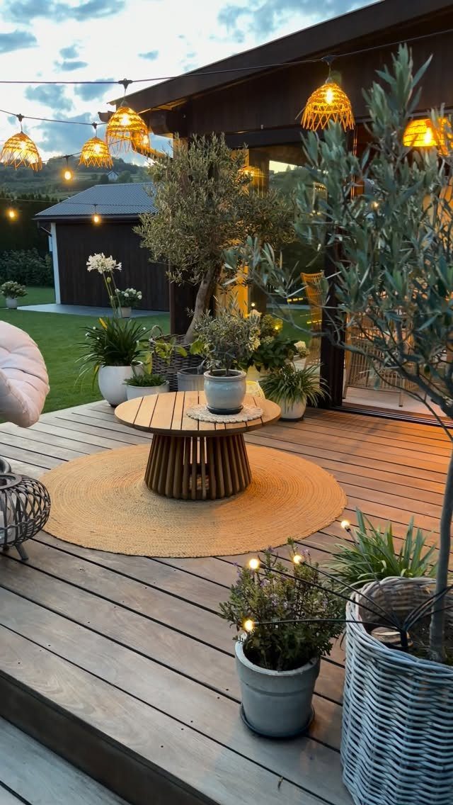Potted plants and woven lanterns decorate a wooden deck with a round coffee table.