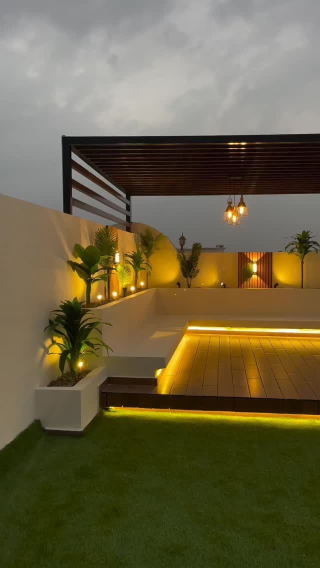 Modern wooden deck illuminated by warm LED strip lighting, hanging pendants, and glowing wall sconces at dusk.