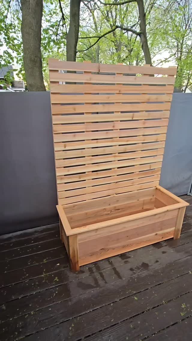 A light cedar wood planter box with a tall slatted trellis standing on a dark deck.