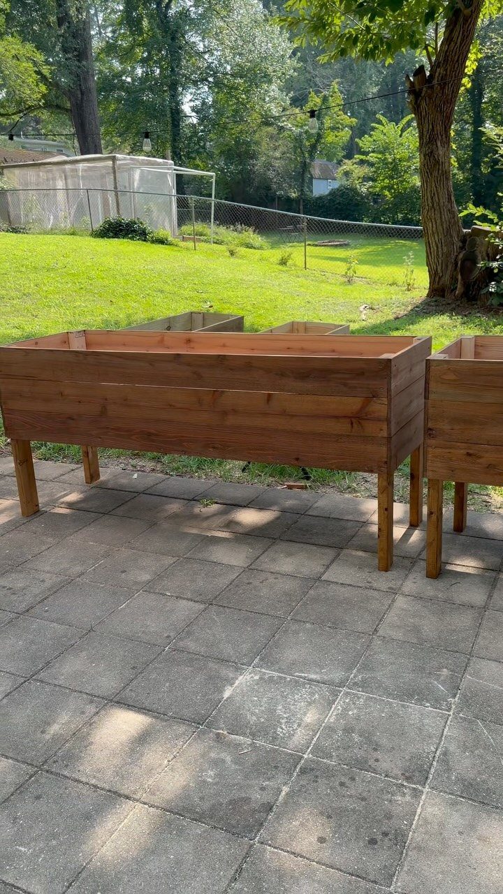 A long cedar wood raised garden bed elevated on legs on a stone patio.