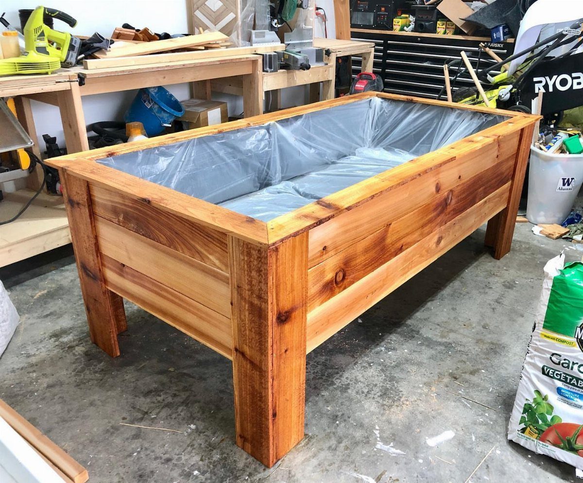 A rectangular cedar raised garden bed lined with plastic sitting in a workshop.