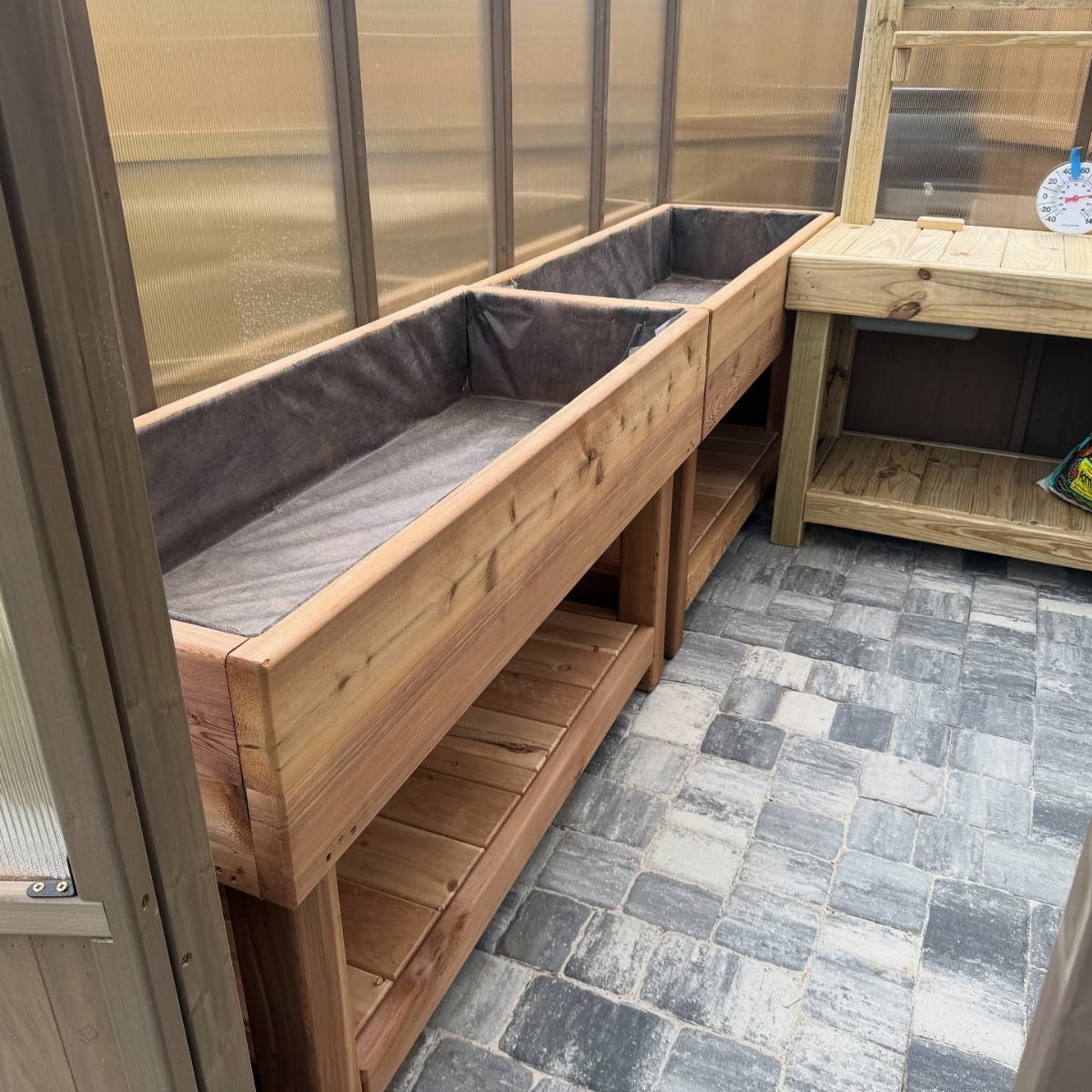 Two waist-high cedar garden beds lined with fabric sitting on a stone patio.