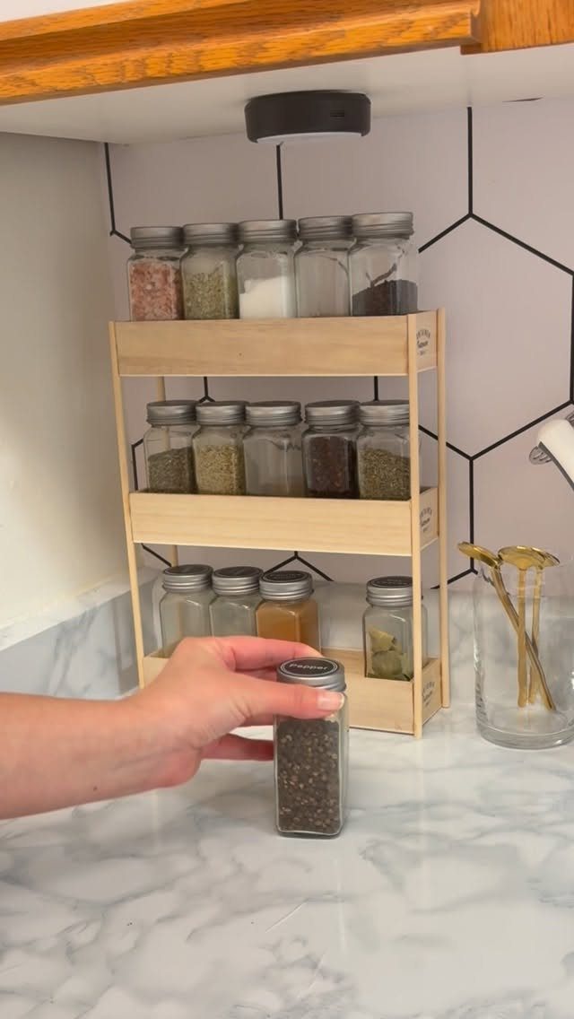 5 DIY Kitchen Ideas for Storage That Actually Fits Your Space 2 A wooden three-tier spice rack filled with glass jars on a marble kitchen countertop.