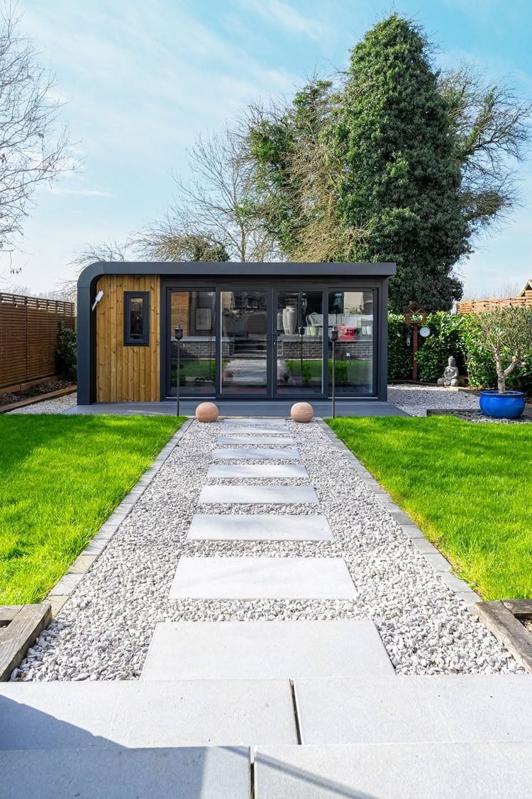Modern garden room with glass doors at the end of a stone and gravel walkway.
