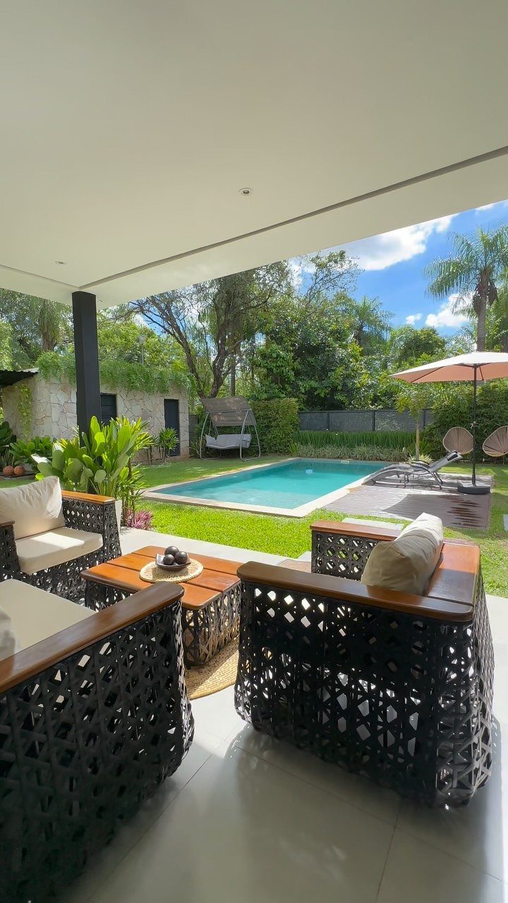 Black woven outdoor armchairs with white cushions arranged on a patio overlooking a swimming pool.