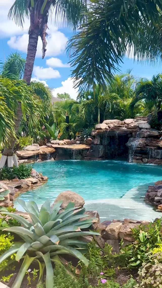 A tropical backyard featuring a turquoise natural pool with rock formations and waterfalls.