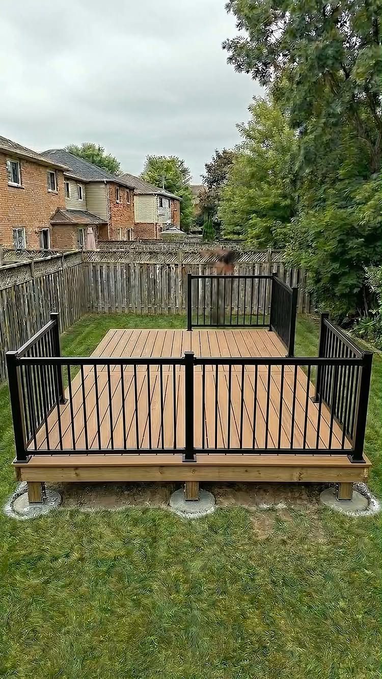 A new wooden outdoor deck with black metal railings installed on a green grass lawn.