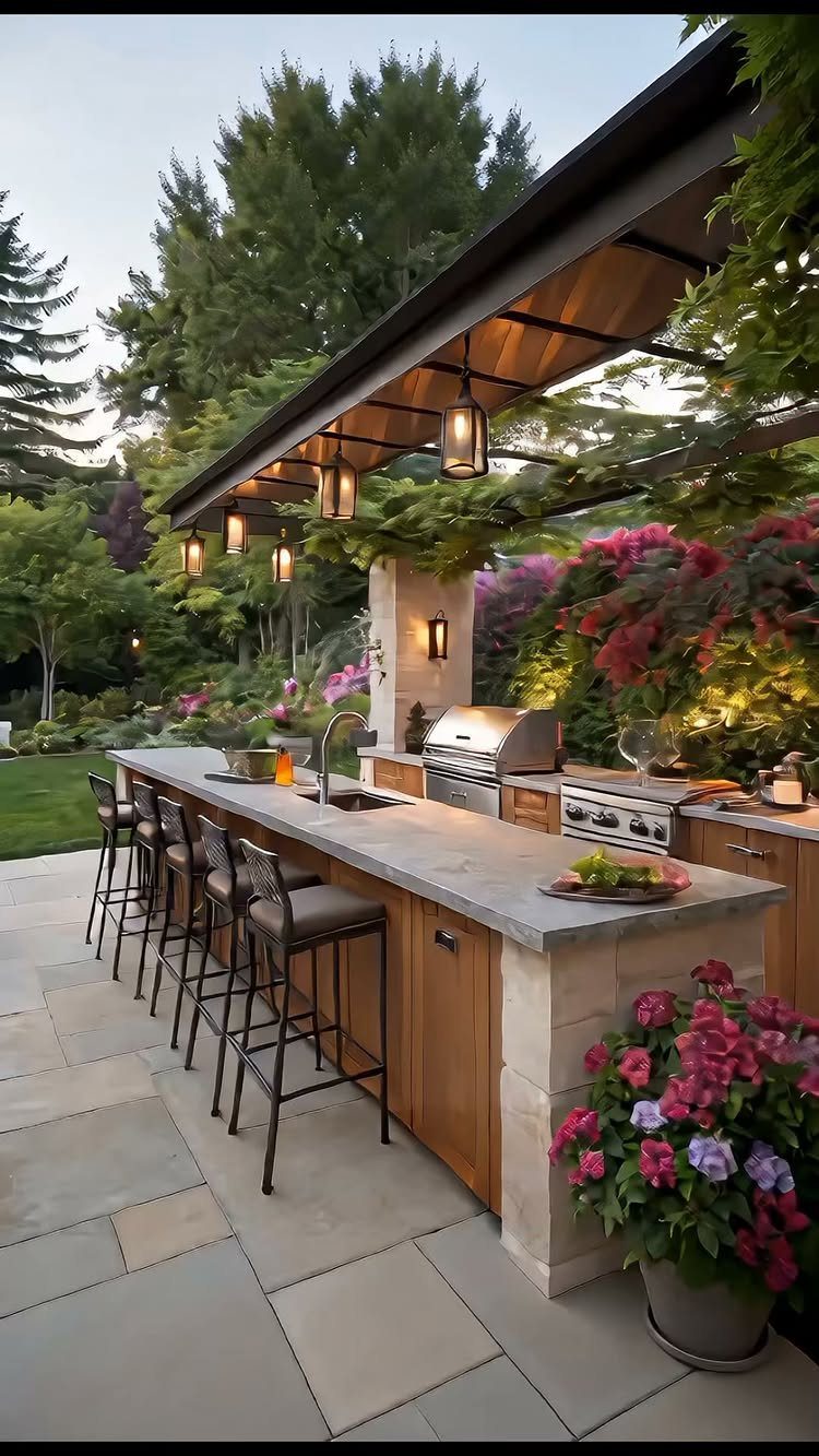 An outdoor kitchen with a stone countertop, built-in grill, and bar stools under a lit pergola.