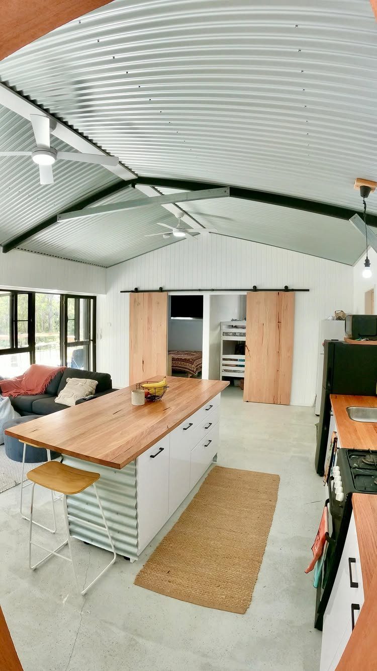 10 Ideas for Farmhouse Shed Home Style 8 Modern interior of a farmhouse shed home with a metal ceiling, wooden kitchen island, and sliding barn doors.