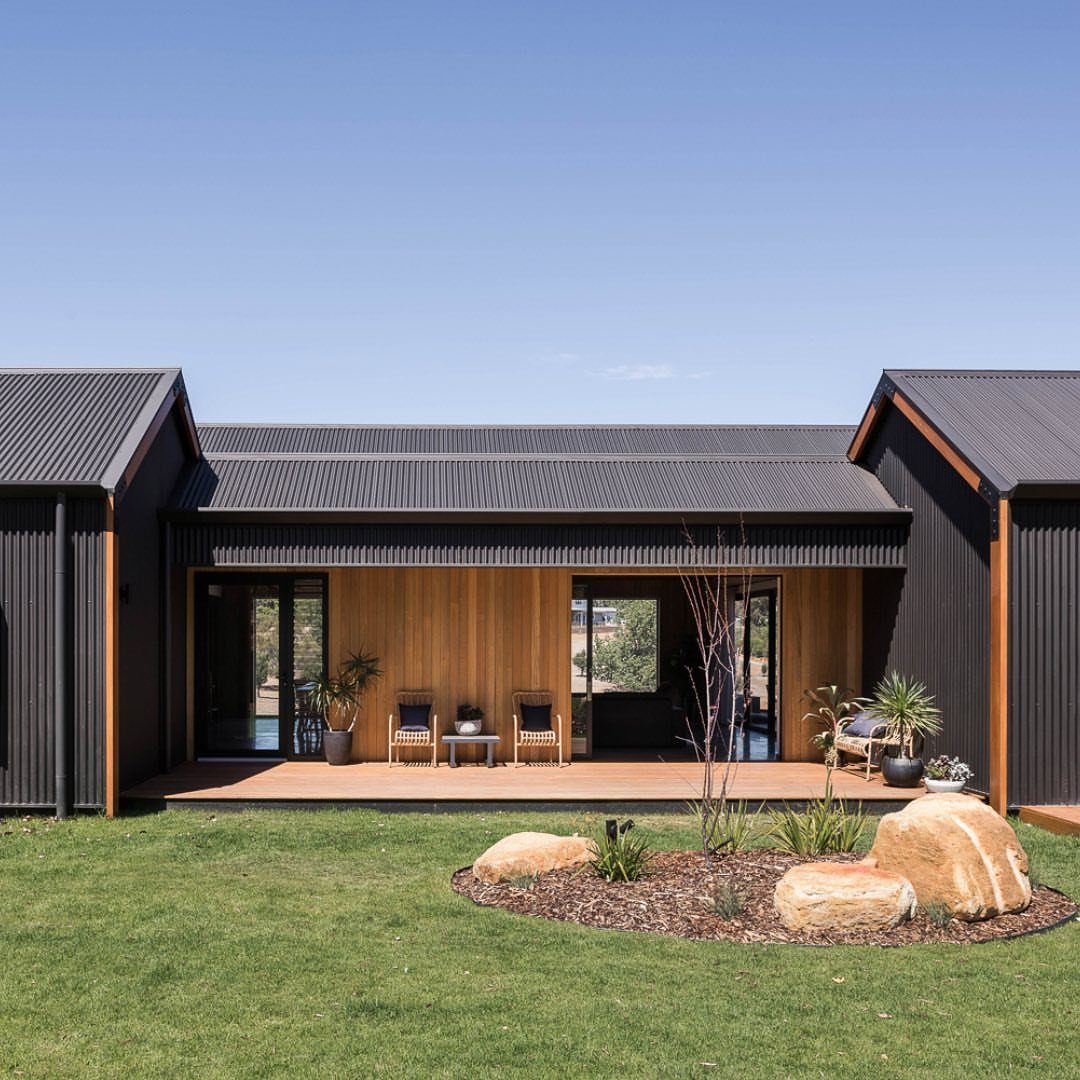 10 Ideas for Farmhouse Shed Home Style 4 Modern farmhouse shed with dark metal siding, wood paneling, and a wooden deck overlooking a lawn.