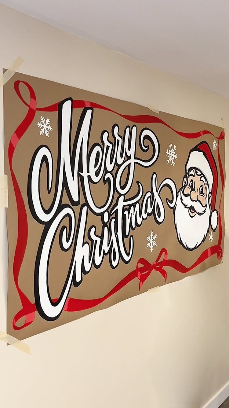 A large tan Christmas banner with Santa Claus and Merry Christmas text taped to a wall.
