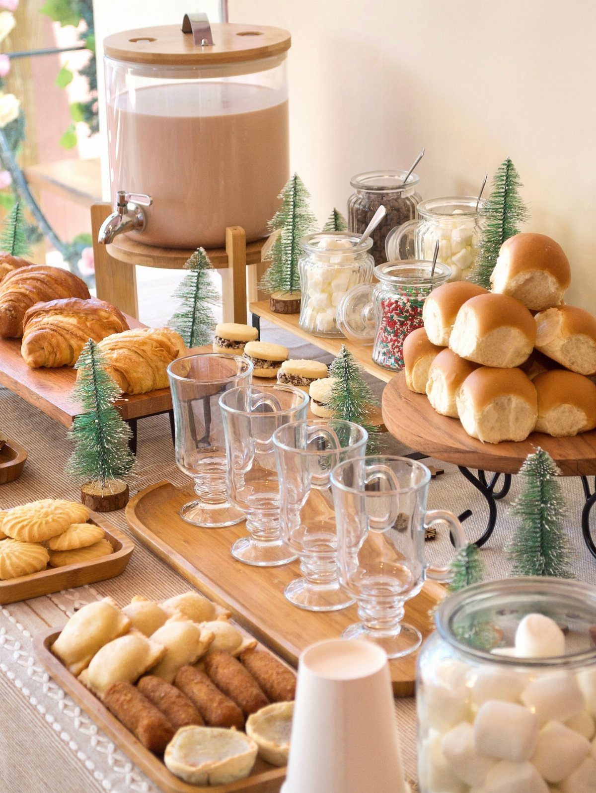 A festive hot cocoa bar with a large chocolate dispenser, pastries, and jars of marshmallows.