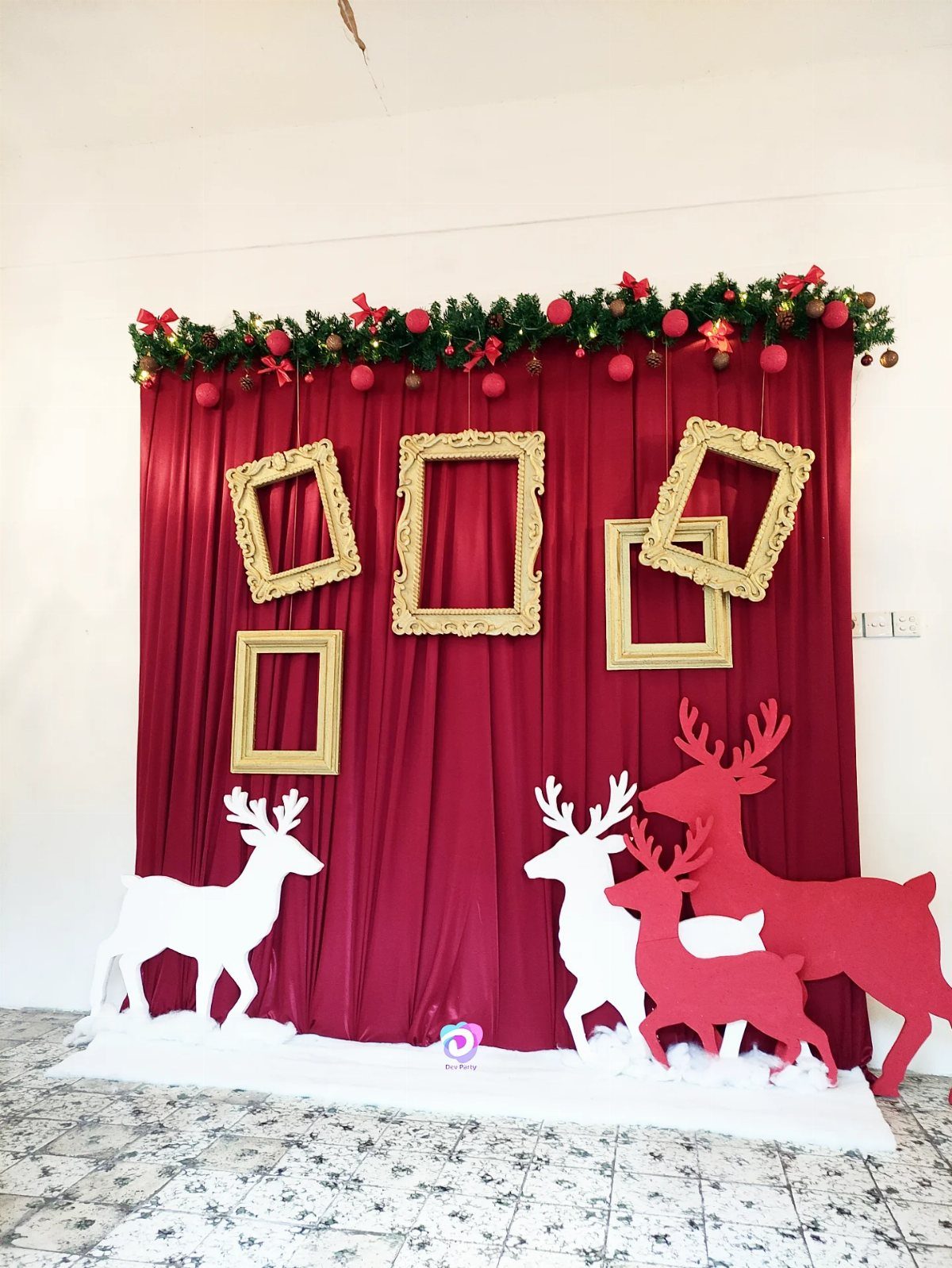Red curtain backdrop with hanging gold frames and reindeer cutouts on a snowy floor.