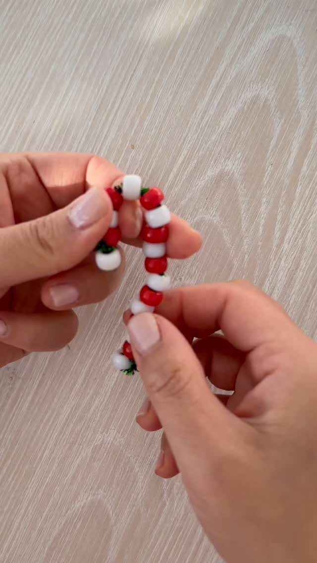 Hands holding a small candy cane ornament made from red and white beads.