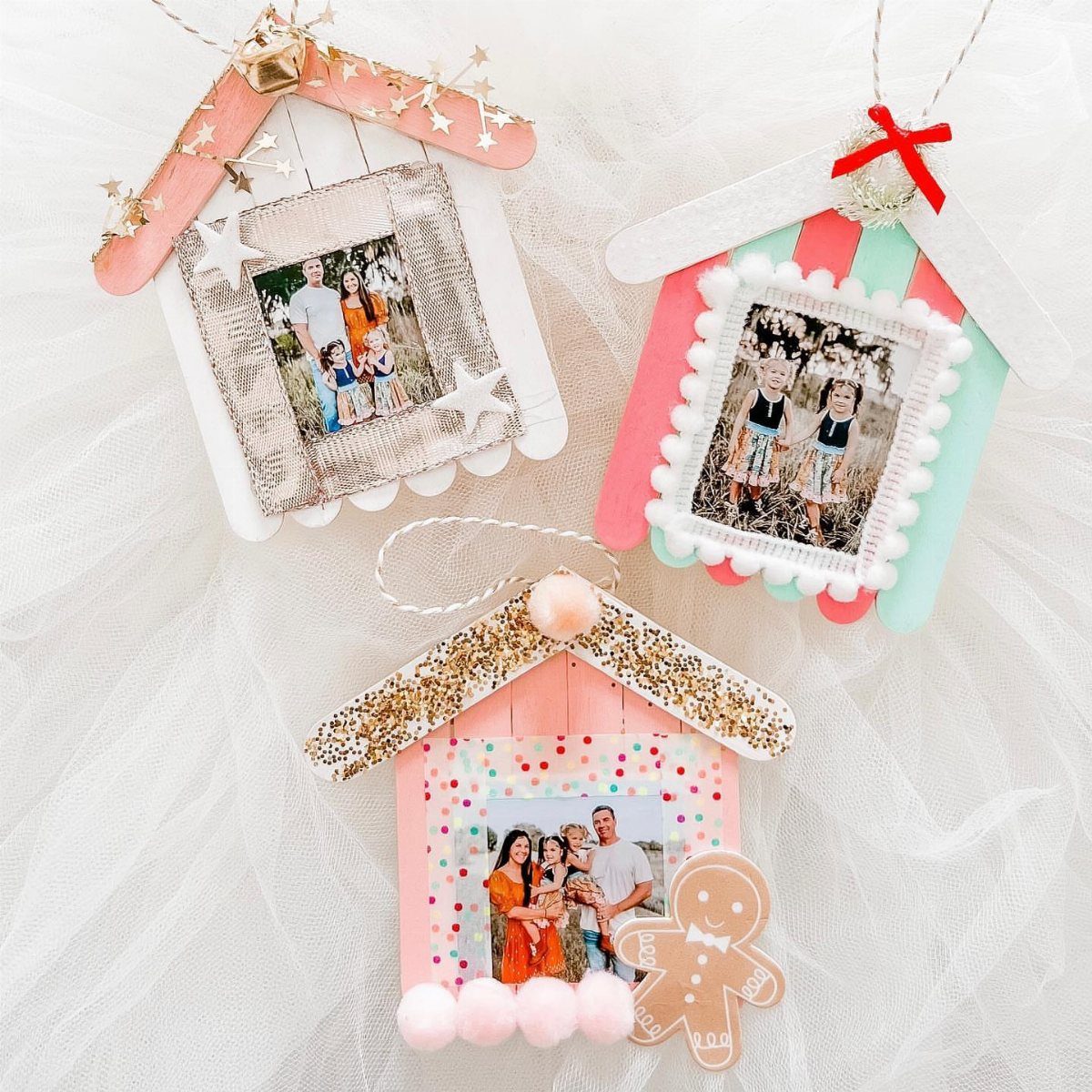 Three handmade house-shaped photo ornaments decorated with glitter and pom-poms on white tulle.