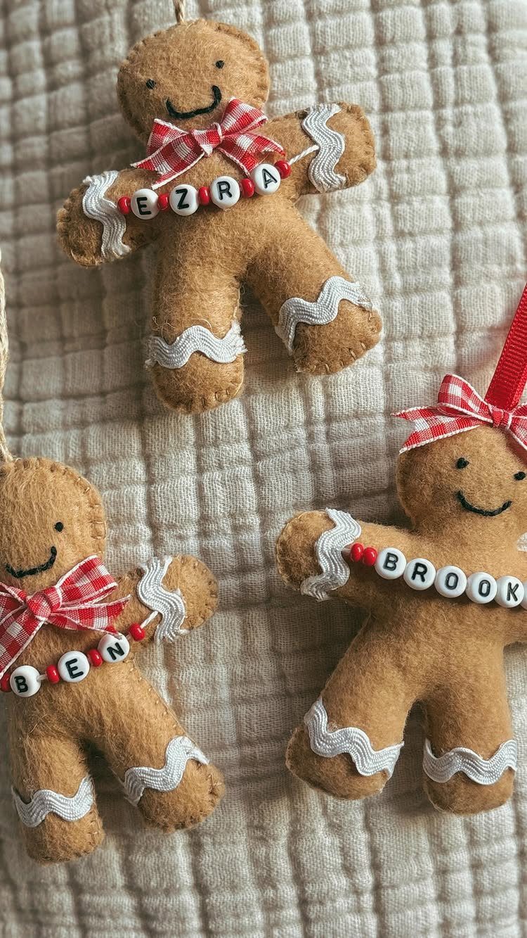 Three tan felt gingerbread man ornaments with red bows and personalized letter beads hanging on fabric.