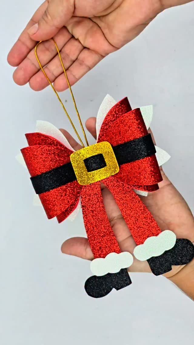 A person holding a red glittery bow ornament styled as Santa Claus with a gold buckle.