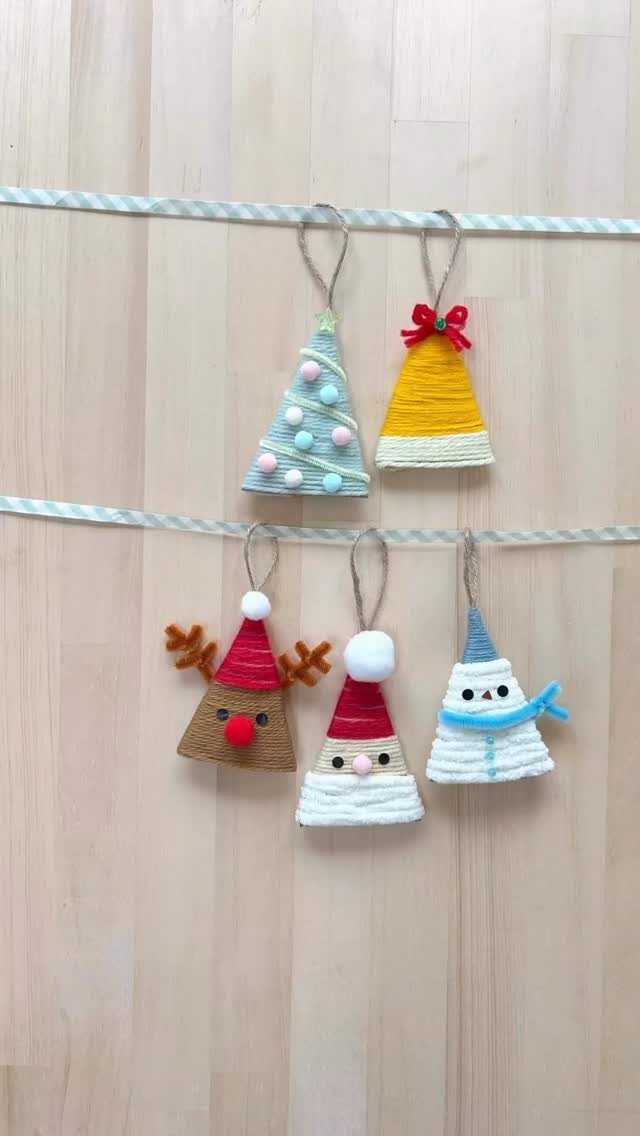 Five colorful yarn-wrapped cone ornaments hanging from white ribbons against a wooden wall.