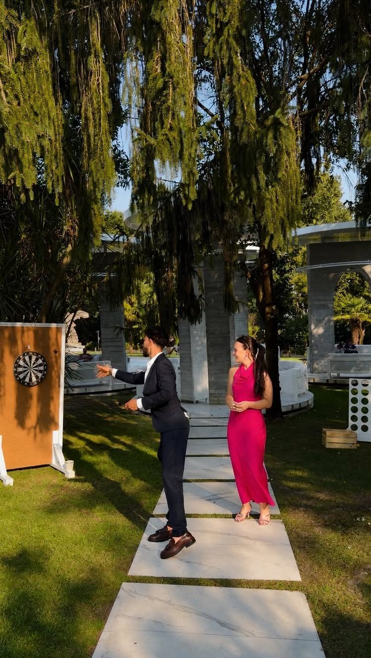 A man throwing a dart at a dartboard while a woman watches him outdoors.