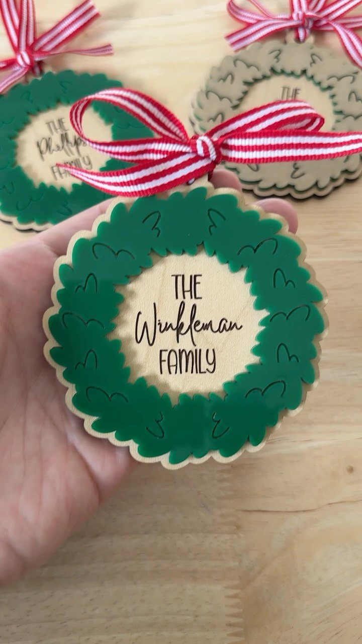 A hand holding a green wreath ornament engraved with the name The Winkleman Family.