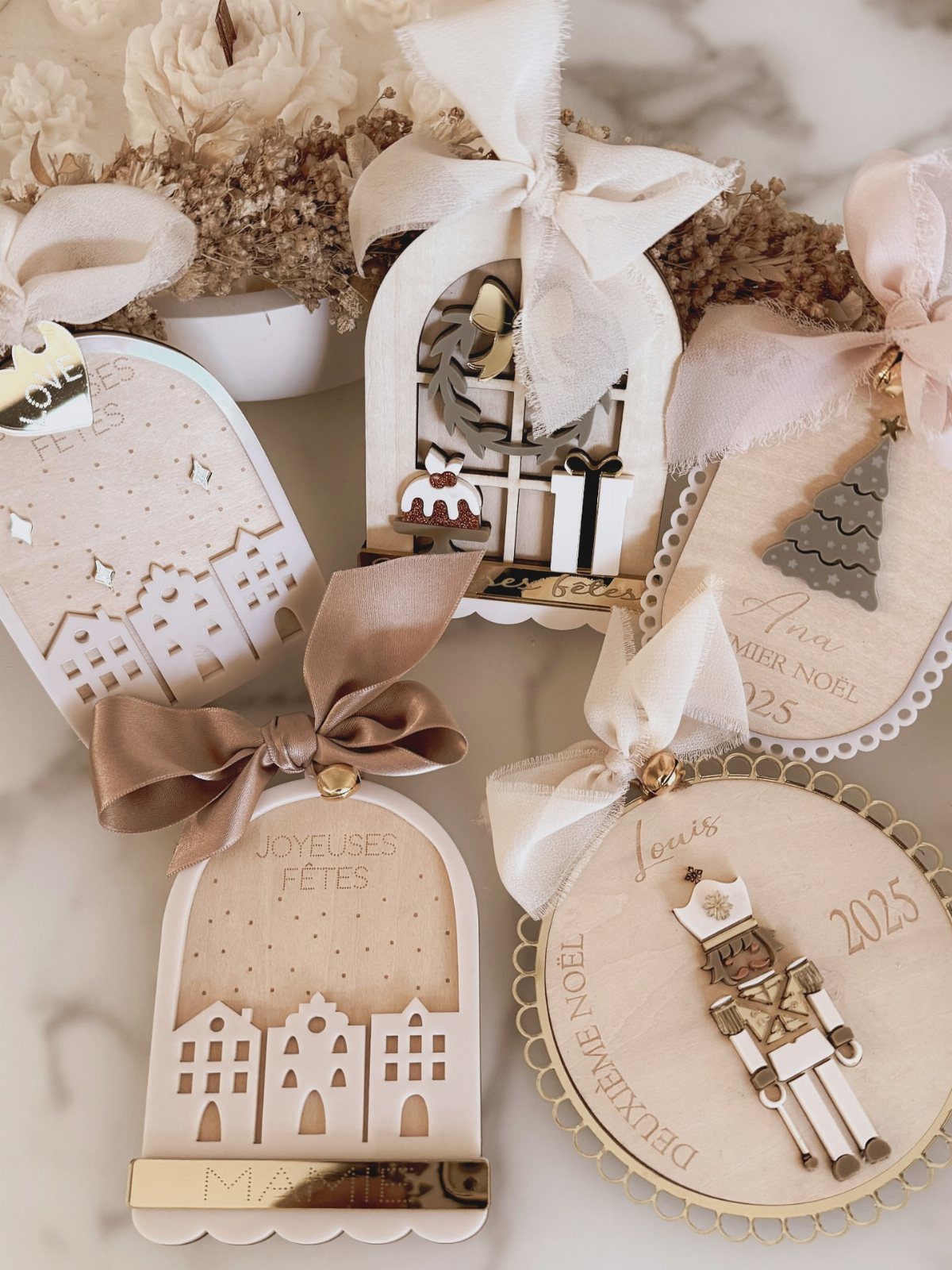 Various laser-cut wooden Christmas ornaments with bows and engraved designs on a marble surface.