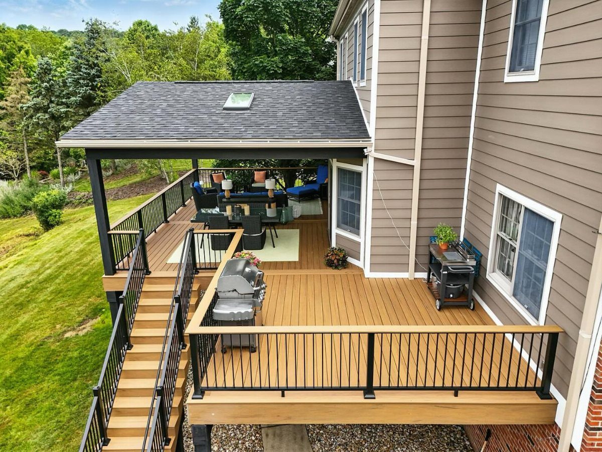 12 Porch and Deck Ideas for Outdoor Living 4 A large wooden deck with a covered dining area and black metal railings attached to a house.
