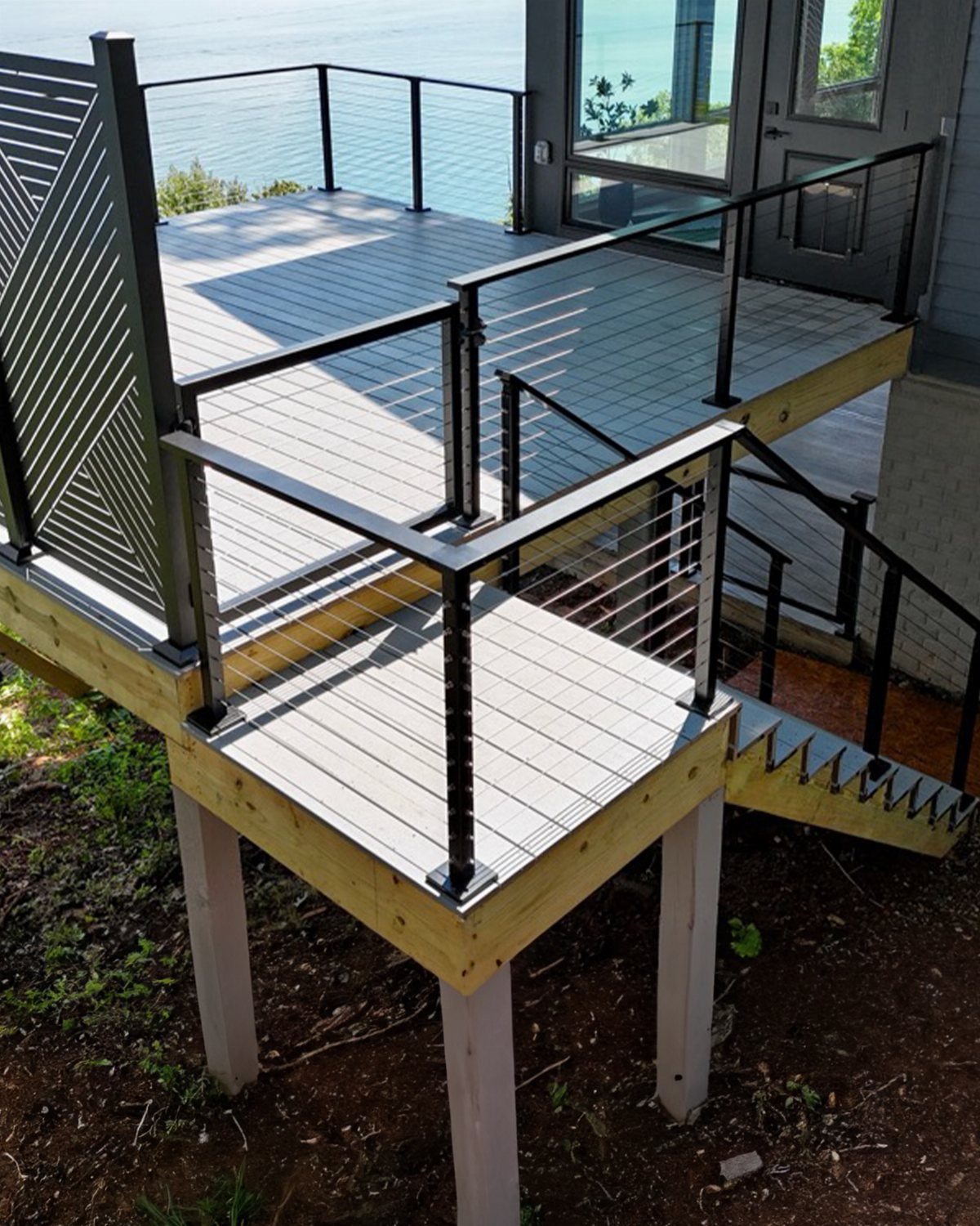 12 Porch and Deck Ideas for Outdoor Living 7 A multi-level wooden deck with grey flooring and modern black cable railings overlooking water.