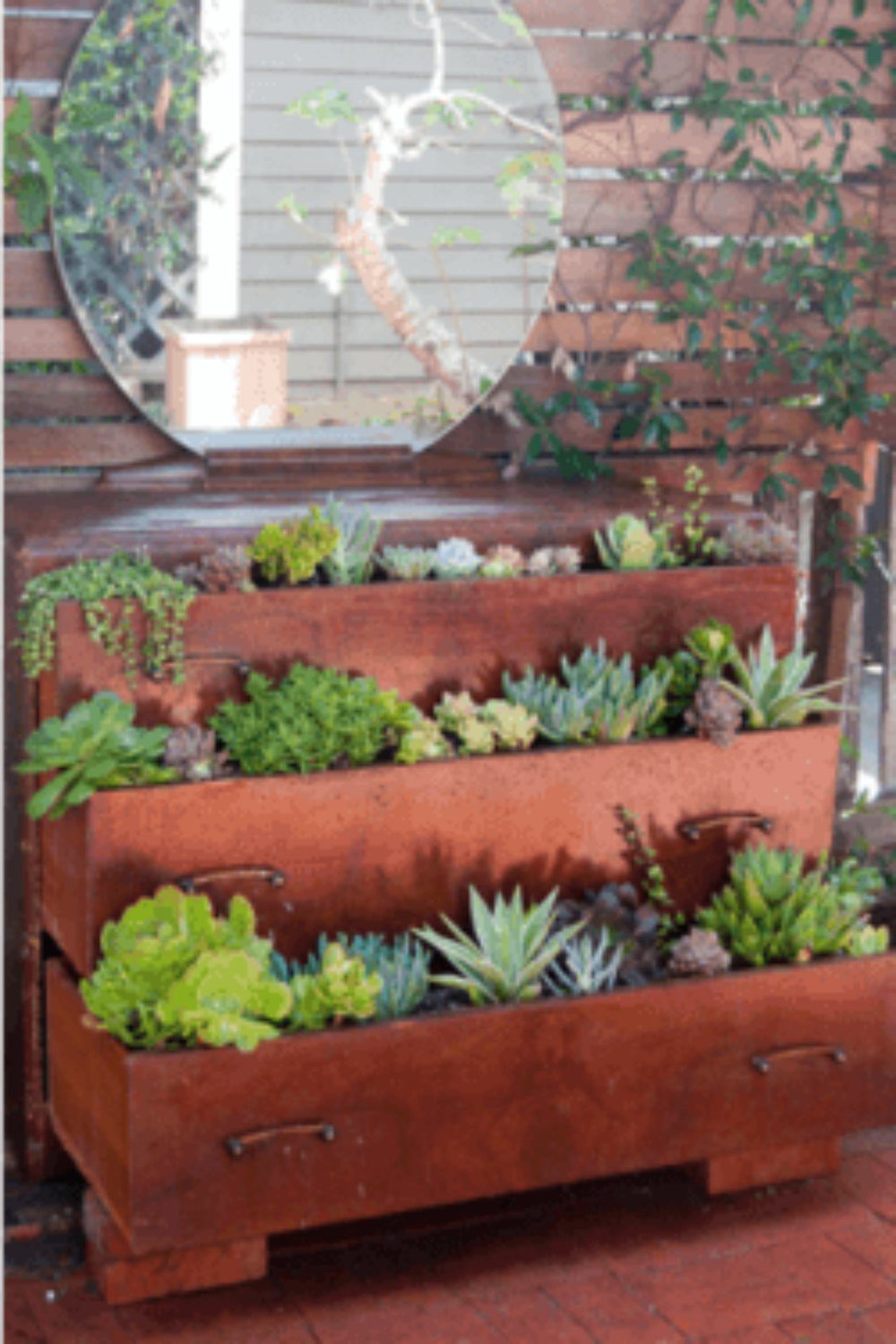 9 Raised Garden Ideas DIY Crafters Build from Scrap and Stone 2 Three large wooden drawers filled with green succulents arranged in a tiered planter setup outdoors.