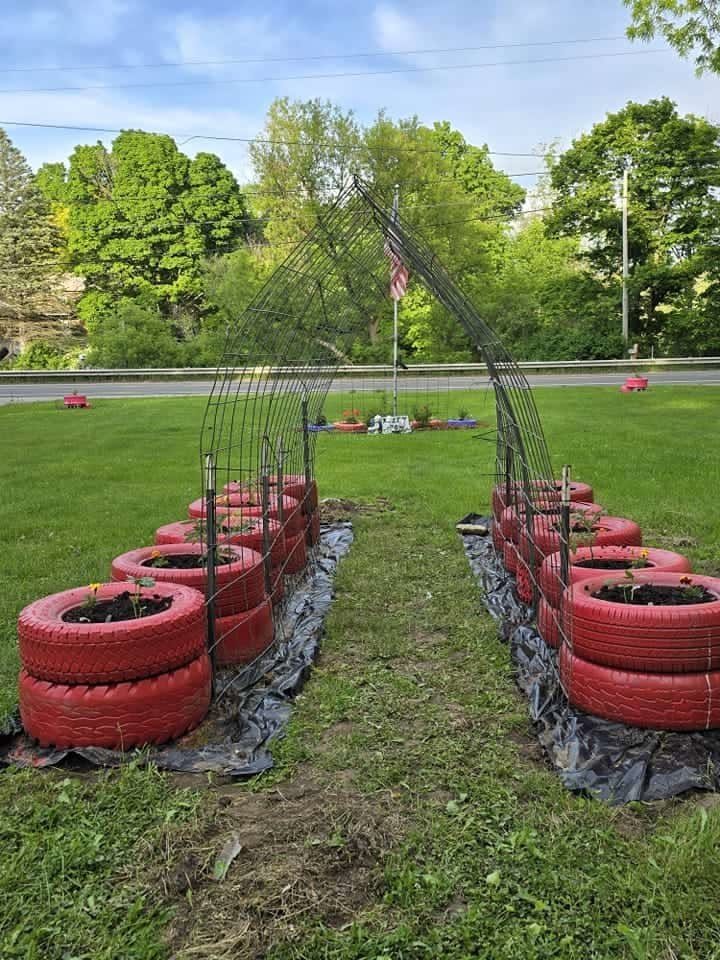 9 Raised Garden Ideas DIY Crafters Build from Scrap and Stone 5 Red stacked tires arranged in rows under a large wire mesh garden arch.