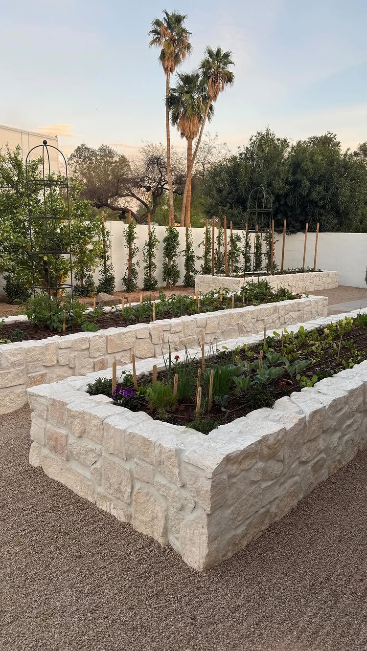 9 Raised Garden Ideas DIY Crafters Build from Scrap and Stone 7 Stacked stone raised garden beds filled with green plants on a gravel patio.