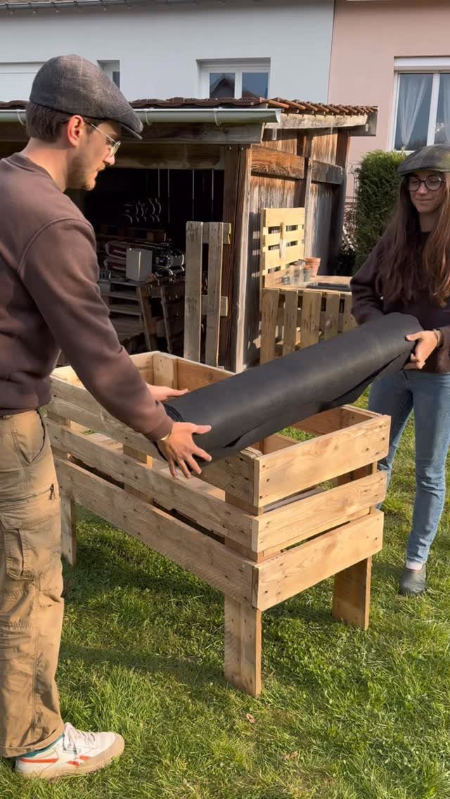 6 Raised Herb Garden Ideas for Every Space and Skill Level 1 Two people lining a wooden planter box with black fabric on a green lawn.