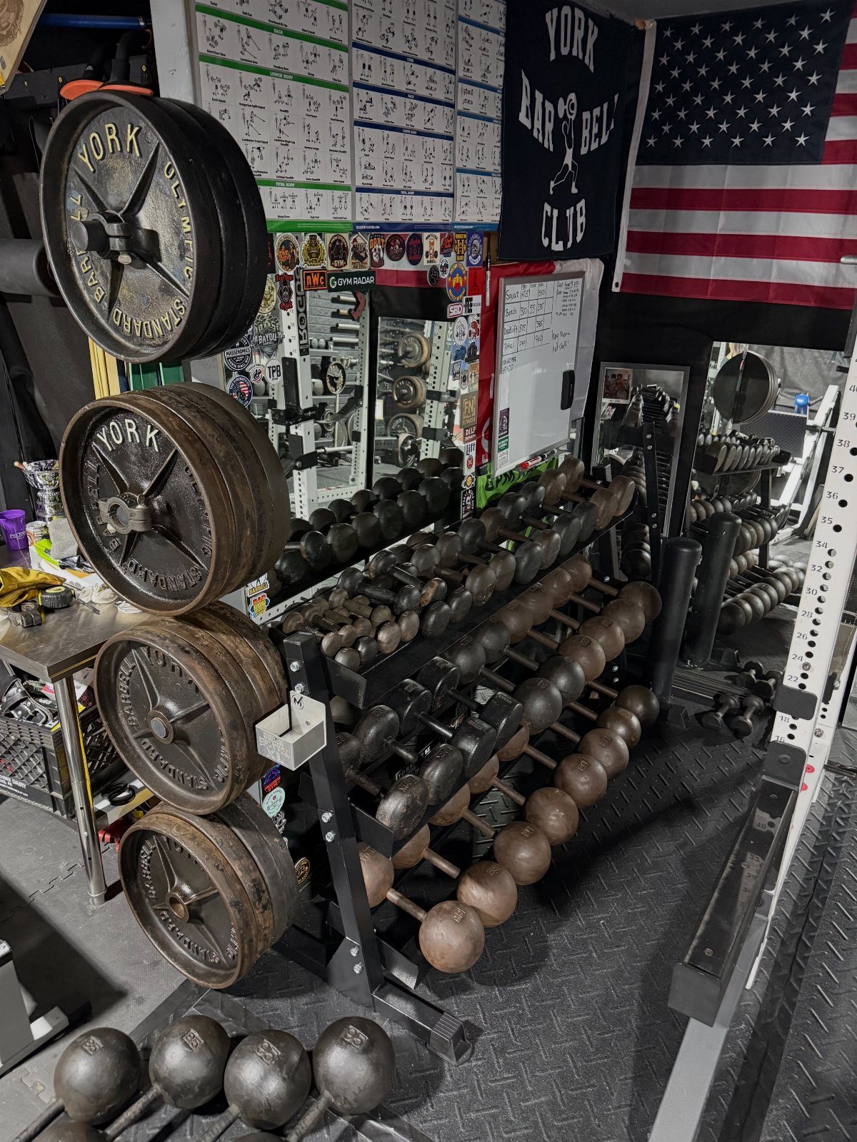 6 Small Garage Building Ideas for Storage, Projects & Living Space 5 Iron weight plates and rows of dumbbells on a storage rack in a garage gym.
