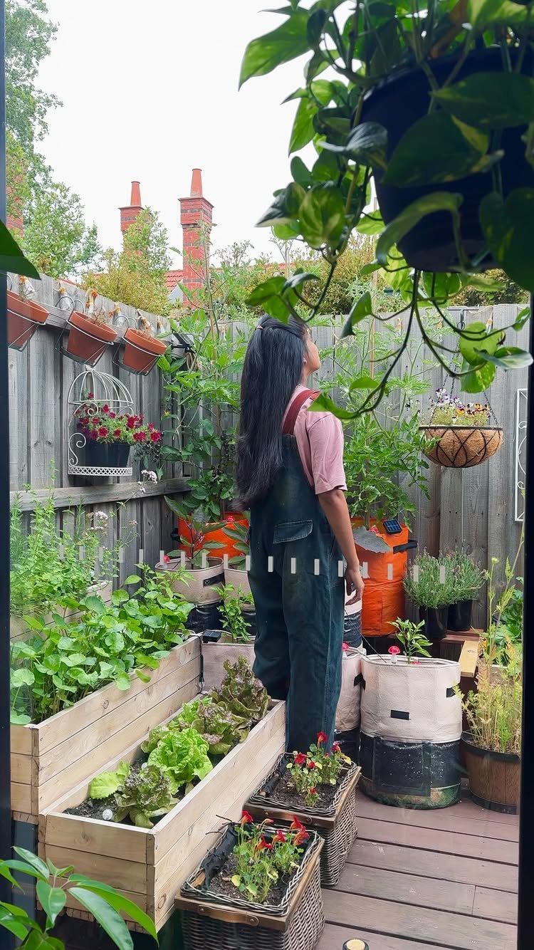 A person standing amidst various potted plants and raised garden beds on a wooden deck.