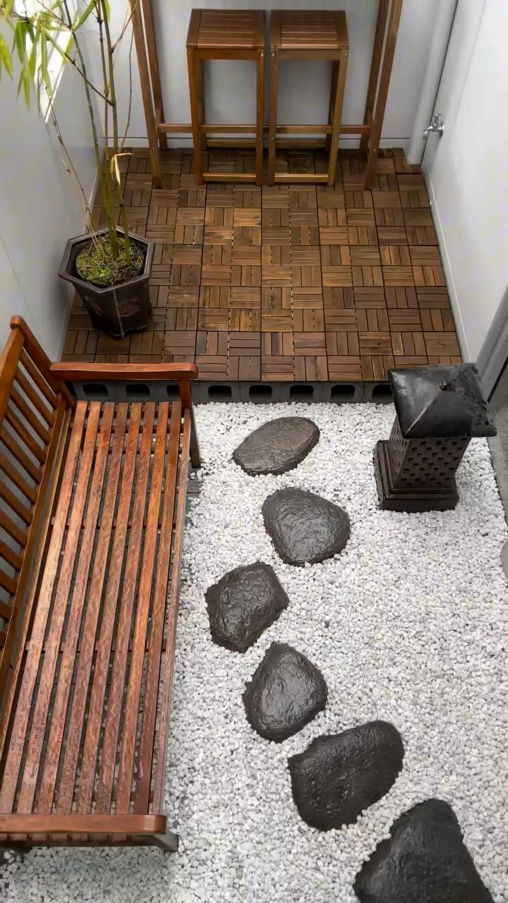 A small Zen garden with white gravel, dark stepping stones, a wooden bench, and a stone lantern.