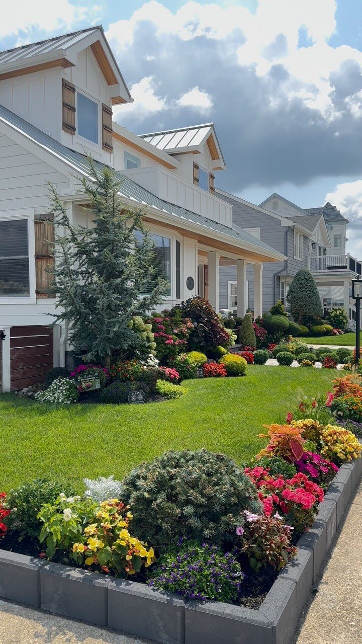 A manicured front yard with colorful flower borders and a green lawn in front of a white house.