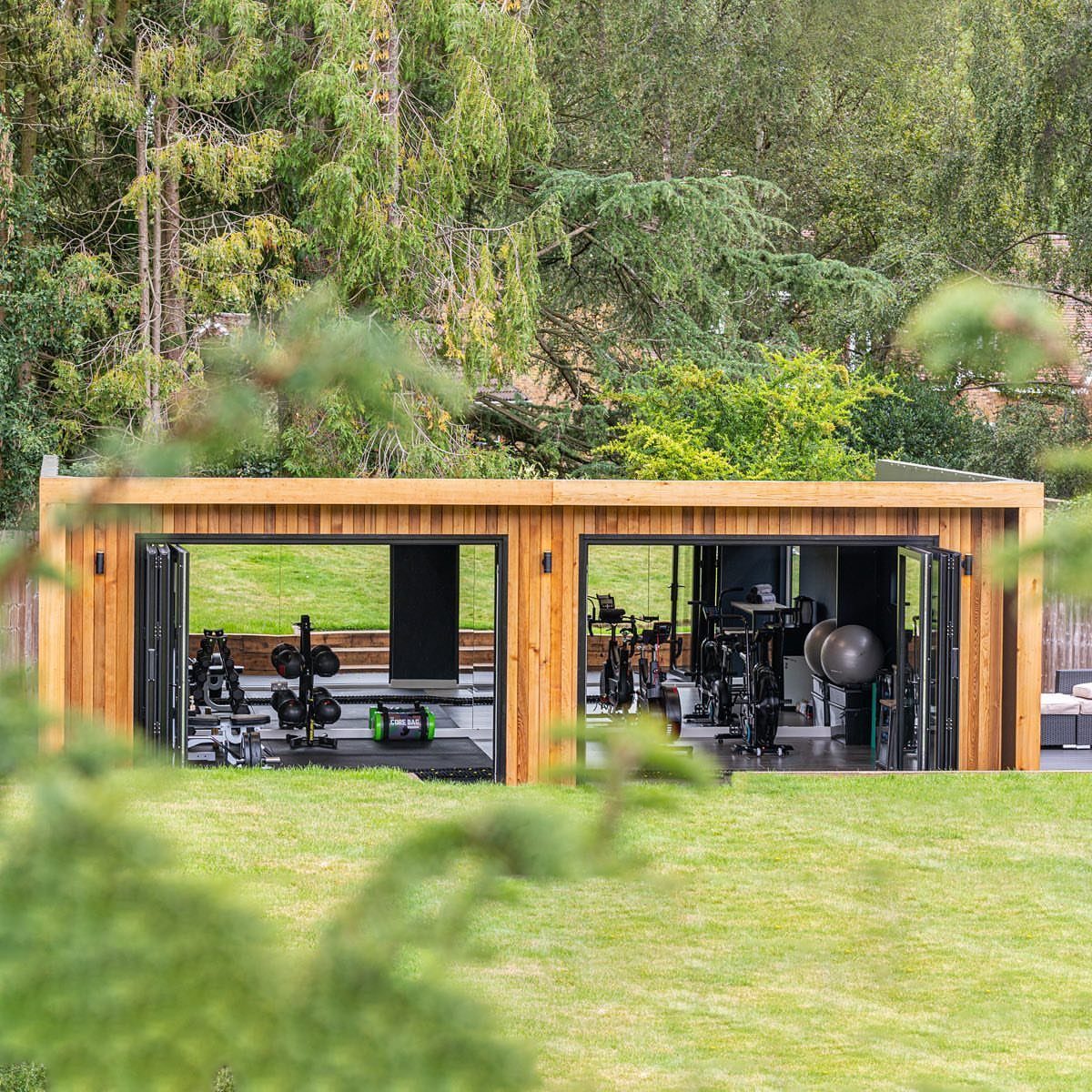 A wooden garden gym building with open doors showing exercise equipment inside.