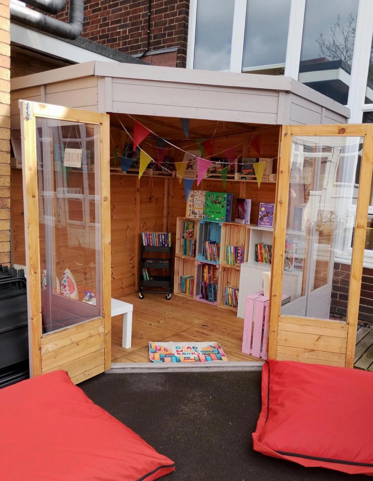 Interior of a wooden garden shed set up as a colorful children's playroom with books and bunting.