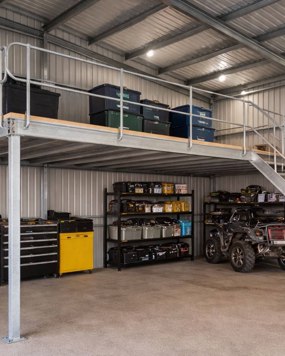 A metal workshop with a raised wooden lofted platform holding various plastic storage bins above garage equipment.