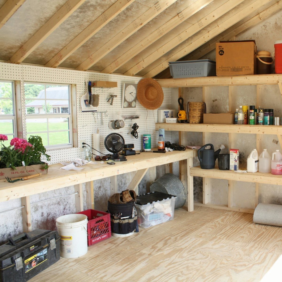 Interior view of a wooden workshop shed with a workbench, pegboard, and shelving units.