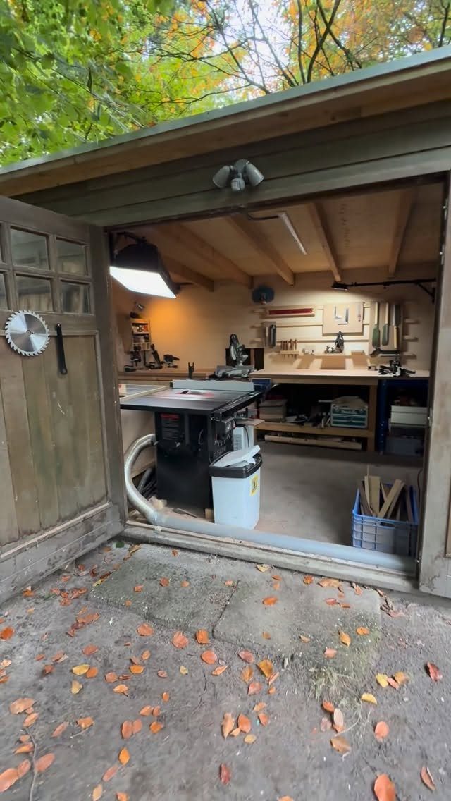 A woodworking workshop inside an open shed with a table saw and various tools.